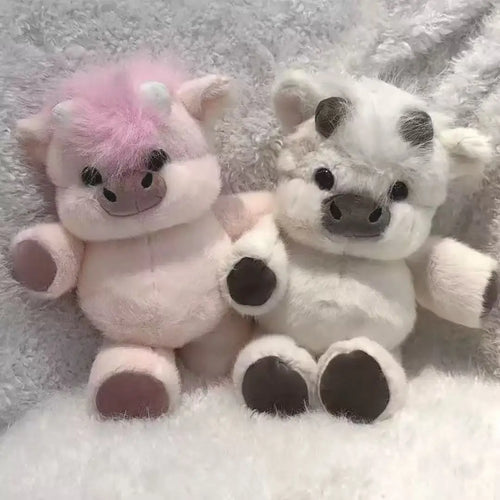 Two plush toys, one pink and one white with black accents, sitting on a textured surface.