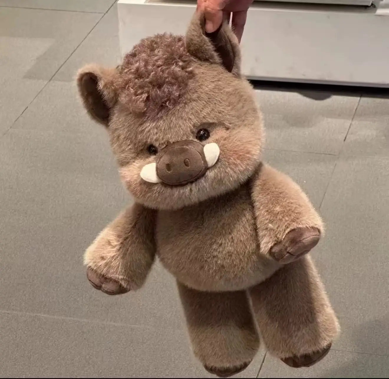 Plush toy resembling a boar held by a hand on a tiled floor.
