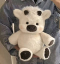 White teddy bear with black paws held by a person wearing a denim jacket.